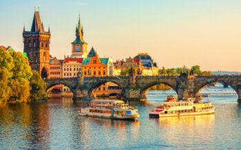 Abendliches Prag mit Karlsbrücke und vorbeigleitenden Ausflugsschiffen – malerische Kulisse für eine unvergessliche Städtereise Prag
