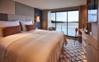 Helle Doppelkabine der Viva Two mit großem Panoramafenster, bequemem Doppelbett und Blick auf die vorbeiziehende Flusslandschaft