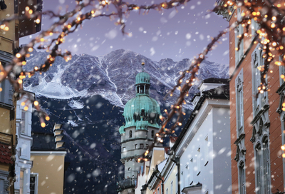 Winterlicher Stadtturm in Innsbruck vor schneebedeckten Alpen bei Schneetreiben und Lichterschmuck – Ausflugsziel bei der Silvesterreise nach Tirol.