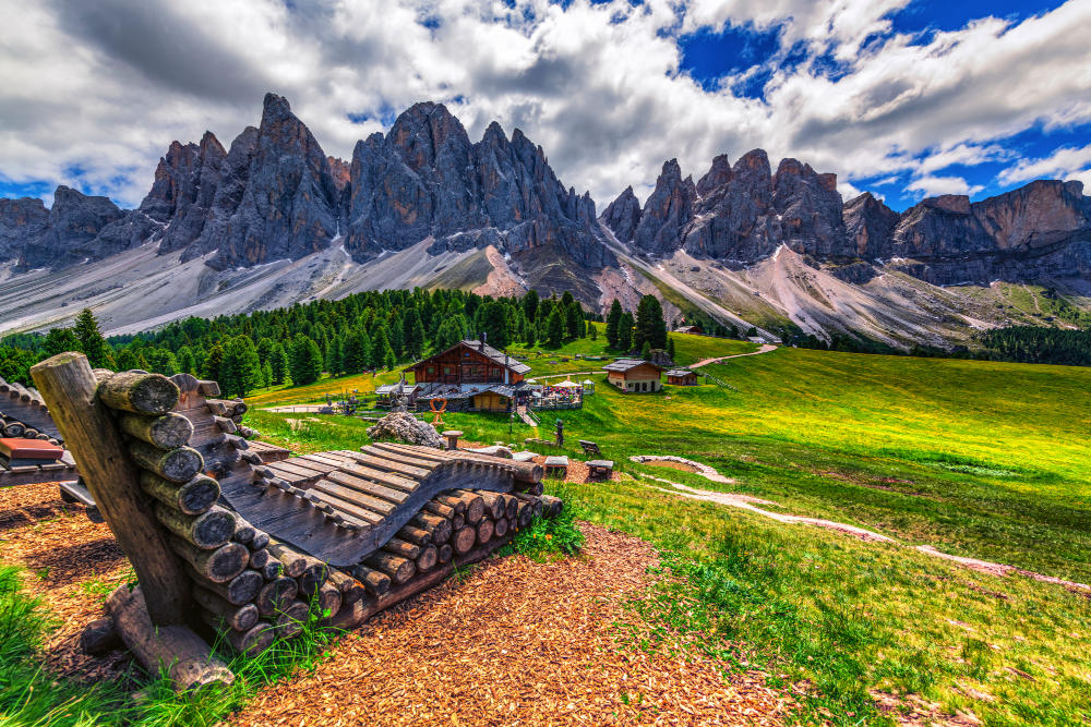Traditionelle Almhütte auf einer grünen Bergwiese vor den markanten Felsgipfeln der Dolomiten in Südtirol