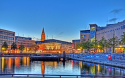 Bunte Stadtszene mit Hafen und reflektierenden Lichtern bei Dämmerung.
