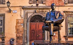 Bronzestatue eines sitzenden Mannes vor einem alten Gebäude mit Holztür.
