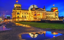 Reichstagsgebäude mit Weihnachtsbaum und Spiegelungen im Wasser am Abend.