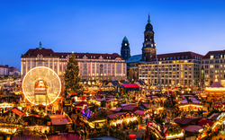 Weihnachtsmarkt bei Nacht mit beleuchteten Ständen und Riesenrad im Hintergrund