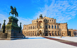 Dresdner Semperoper im Winter mit Schnee auf dem Theaterplatz und einer Statue im Vordergrund.