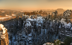 Verschneite Sandsteinfelsen und Brücke im Morgenlicht in einer Berglandschaft.
