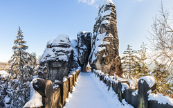Verschneite Felsenbrücke in winterlicher Landschaft mit verschneiten Bäumen und klarem Himmel.