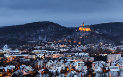 Winterliche Stadtansicht mit beleuchtetem Schloss auf einem Hügel.