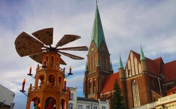 Kirchturm und Weihnachtsmarkt mit Holzpyramide bei Tageslicht.