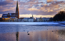 Stadtansicht im Winter bei Sonnenuntergang mit Kirche und zugefrorenem See.