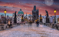 Menschen spazieren bei Schneefall über die Karlsbrücke in Prag bei Sonnenuntergang.