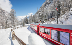 Roter Zug fährt durch verschneite Berglandschaft.