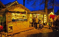 Weihnachtsmarkt am Abend mit beleuchteten Holzbuden und Besuchern.
