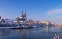 Verschneite Stadtlandschaft mit Fluss und gotischer Kathedrale.