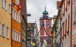 Schmale Altstadtgasse mit bunten Häusern und Kirchturm im Hintergrund.