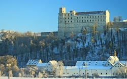 Schloss auf Hügel mit Bäumen im Winter, Schnee bedeckt die Dächer der Gebäude.