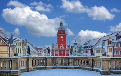 Marktplatz mit rotem Turmgebäude, umgeben von bunten Häusern im Winter.