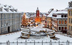 Verschneiter Marktplatz mit Weihnachtsbaum und festlich beleuchteten Gebäuden.