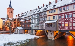 Mehrstöckige Fachwerkhäuser überbrücken im Winter ein kleines Gewässer.