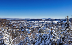 Verschneite Winterlandschaft mit bewaldeten Hügeln und blauem Himmel im Hintergrund