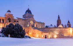 Historisches Gebäude im Winter mit Schneebedeckung und Beleuchtung bei Dämmerung.
