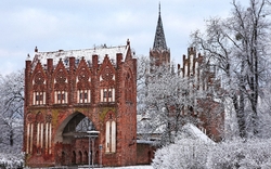 Gotisches Backsteinbauwerk im Winter, umgeben von schneebedeckten Bäumen.