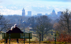 Älteres Paar sitzt auf einer Bank mit Blick auf eine Stadtlandschaft.