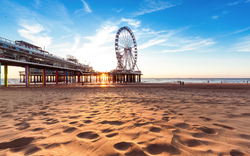 Riesenrad auf einem Pier am Strand bei Sonnenuntergang, mit blauem Himmel und einigen Wolken.