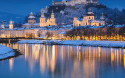 Verschneite Stadt und Festung, ruhig reflektiert in einem Fluss bei Abenddämmerung.