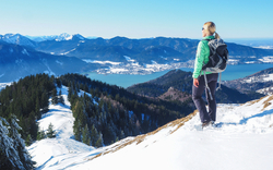 Frau beim Wandern im Winter am Tegernsee in Bayern mit Blick auf die verschneiten Alpen und den See.