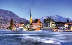 Verschneite Alpenlandschaft mit Dorf und Kirche am See.