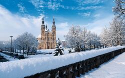 Der Fuldaer Dom im Winter, umgeben von schneebedeckten Bäumen und blauem Himmel.