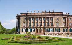 Barockschloss mit gepflegtem Garten und blauen Himmel im Hintergrund.