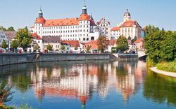 Historisches Schloss an einem Flussufer mit Spiegelung im Wasser.