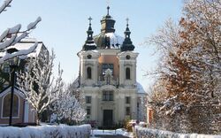 Wallfahrtskirche Christkindl im Winter mit Schnee auf Bäumen und Wegen.