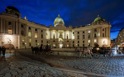 Pferdekutsche vor der beleuchteten Hofburg am Heldenplatz in Wien an einem Winterabend.