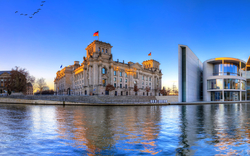 Panoramafoto des Berliner Reichstags und des Kanzleramts am Ufer der Spree bei sonnigem Himmel.