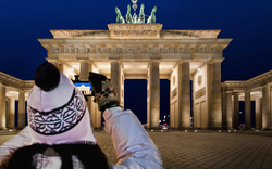 Eine Touristin fotografiert nachts das beleuchtete Brandenburger Tor in Berlin, Deutschland.