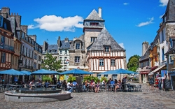 Platz mit hist. Fachwerkhäusern, Cafés, Sonnenschirmen und Menschen bei sonnigem Wetter.