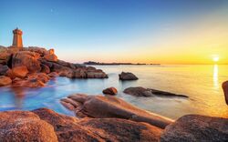 Küste mit Felsen und Turm, Sonnenuntergang über dem Meer.