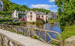 Fluss, Steinbrücke und Häuser in einem malerischen Dorf bei Sonnenschein.