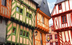 Fachwerkhäuser mit bunten Fassaden in Grün, Orange und Rot in einer historischen Altstadt.