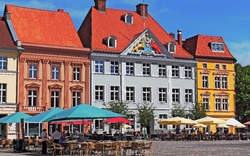 Bunte historische Gebäude mit Straßencafé und Sonnenschirmen.