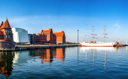 Panorama einer Hafenstadt mit historischen Gebäuden und einem Segelschiff im Wasser.
