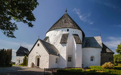 Weiße, runde Kirche mit Schieferdach und blauem Himmel im Hintergrund.