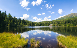See mit Wald und Bergen im Hintergrund unter blauem Himmel mit Wolken.