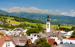 Blick auf malerisches Dorf mit Kirchturm und Bergen im Hintergrund.