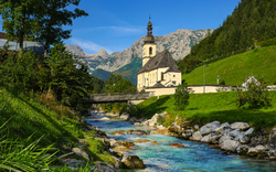 Kirche am Fluss mit Bergen im Hintergrund bei klarem Himmel.