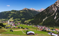Bergdorf in den Alpen mit grünen Wiesen und blauen Himmel im Hintergrund.