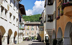 Straße in italienischer Stadt mit historischen Gebäuden und grünem Hügel im Hintergrund